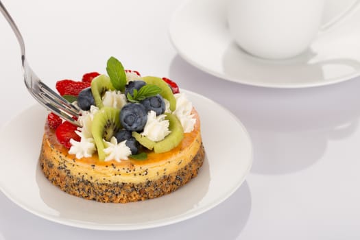 Cheese-cake with strawberries, blueberries, kiwi and cream on white plate.