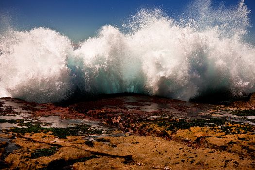 Beautiful natural environmental background of powerful spray from a crashing wave pounding ashore on a rocky ledge at the coast