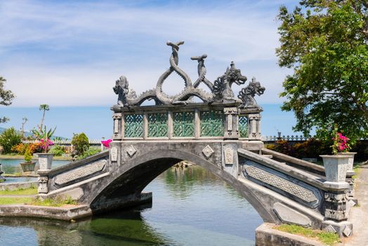 Stone balinese style arch bridge in a park with gragon images, Tirtaganga, Bali