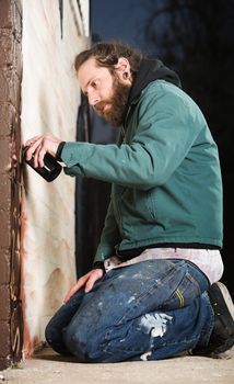 Man kneeling on the ground while spray painting a wall