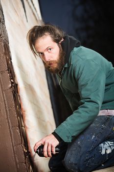 Adult graffit artist next to wall with spray paint can