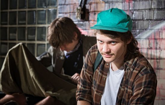 Frustrated young homeless man with friend sitting outside