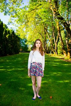 A beautiful young girl poses for a fashion style portrait outdoors at a park with natural lighting.
