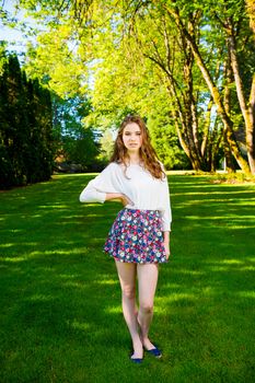 A beautiful young girl poses for a fashion style portrait outdoors at a park with natural lighting.