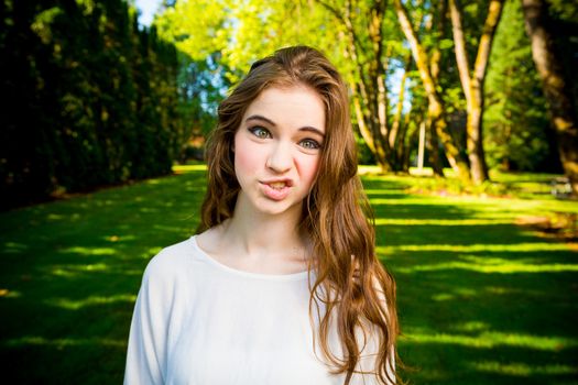 A beautiful young girl poses for a fashion style portrait outdoors at a park with natural lighting.