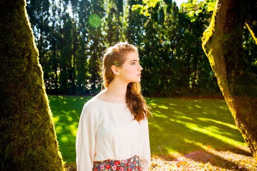 A beautiful young girl poses for a fashion style portrait outdoors at a park with natural lighting.