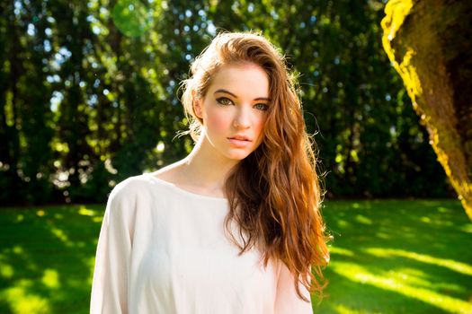 A beautiful young girl poses for a fashion style portrait outdoors at a park with natural lighting.