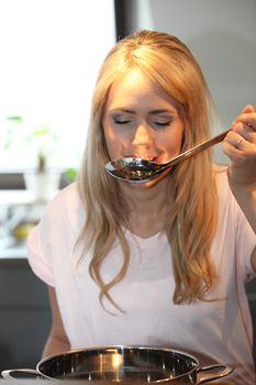 Woman tasting her cooking from the pot using a big stainless steel ladle and closing her eyes in appreciation