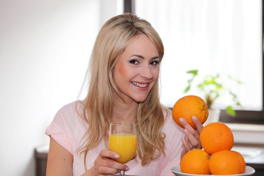 Happy young woman with fresh oranges and a glass of orange juice in her hand smiling at the camera conceptual of a healthy diet and lifestyle