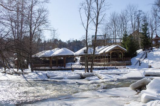 frozen river water and small wooden village houses on bank with roof covered snow in winter.