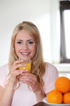 Beautiful young blond woman drinking a glass of fresh orange juice with a bowl of fresh fruit in the foreground
