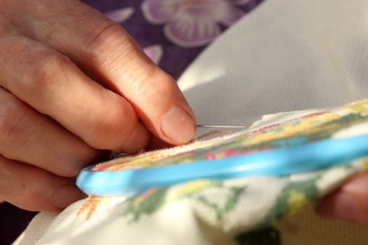 Hands of an old woman busy embroidering