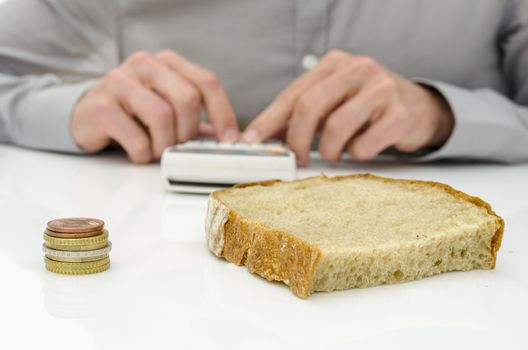 Bread slice and Euro coins on white desk with man calculating food costs in background.