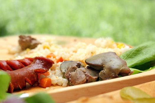 chicken liver and pork sausages served with green salad on wooden plate