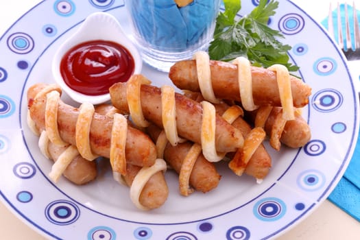 Twisted pastry around chicken sausages with ketchup.