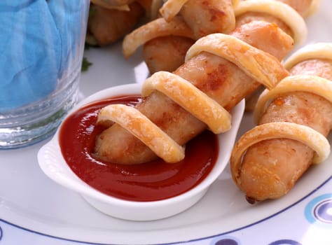 Twisted pastry around chicken sausages with ketchup.