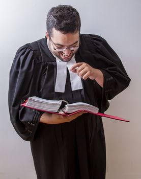 Man in canadian lawyer toga holding a book of law laughing at it