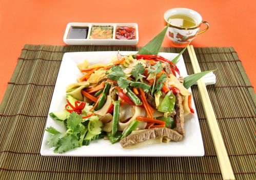 Freshly prepared beef noodle stirfry with condiments and green tea.