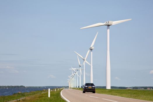 row of wind turbines and car on dike in The Netherlands
