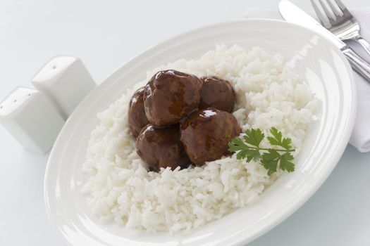 Chinese meat balls in hoisin sauce on a bed of white rice with parsley.