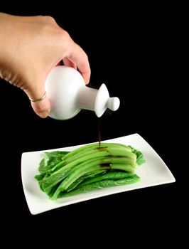 Soy sauce being poured on the Asian vegetable Choy Sum.