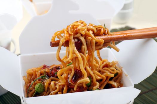 Take away BBQ egg noodles on chopsticks in a take away container.