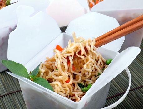 Take away egg noodles on chopsticks in a take away container.