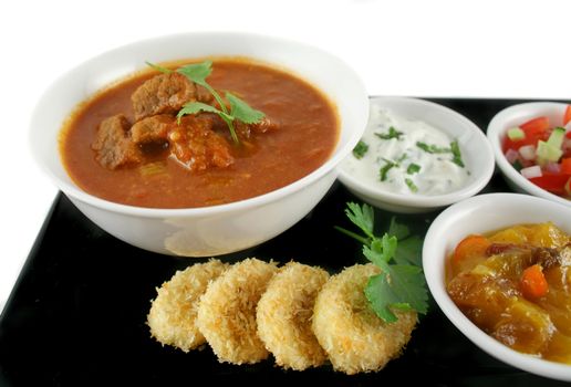 Indian feast of vindaloo curry, mango chutney, banana and coconut, tomato and cucumber.