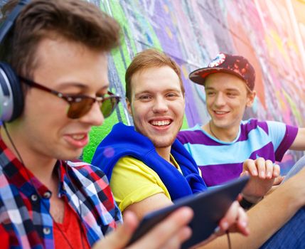Happy teens boy with his friends by painted wall sunrise listening to music.
