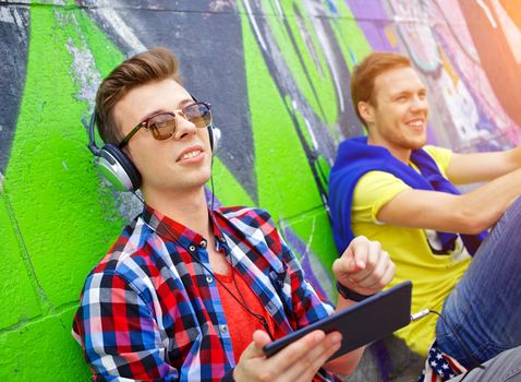 Happy teens boy with his friend by painted wall sunrise listening to music.