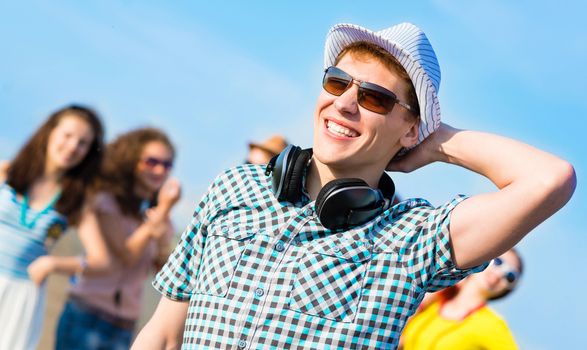 young man in sunglasses, a hat holds a hand on a background of blue sky and friends