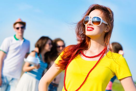 stylish young woman in sunglasses on the background of blue sky and friends