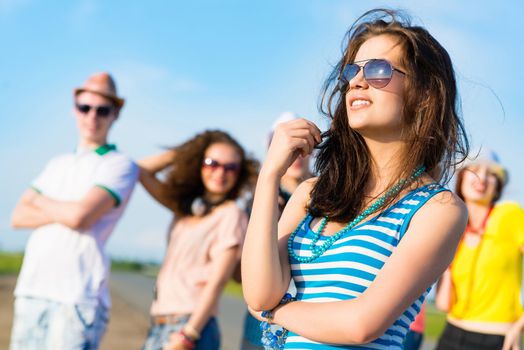 stylish young woman in sunglasses on the background of blue sky and friends