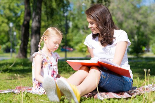 girl with the teacher reading a book together in the summer park