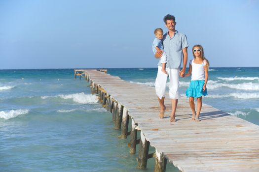 Father with his two kids walking on wooden jetty by the ocean
