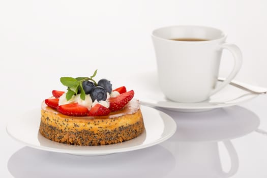 Cheesecake with strawberry, blueberry, mint and cream on white plate with cup of coffee and spoon.