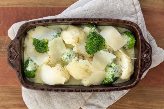 Gratin of cauliflower, broccoli and cheese before cooking in brown rustic dish.