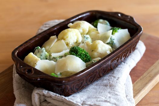 Gratin of cauliflower, broccoli and cheese before cooking in brown rustic dish.