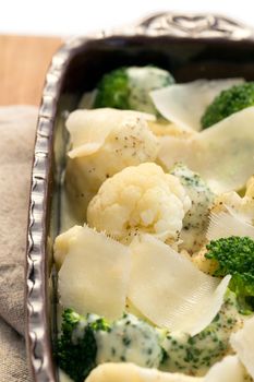 Gratin of cauliflower, broccoli and cheese before cooking in brown rustic dish.