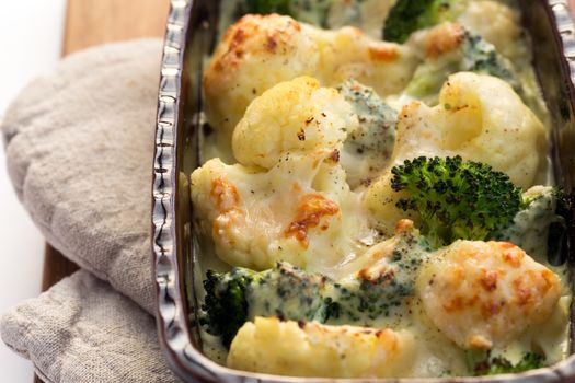 Gratin of cauliflower, broccoli and cheese in brown rustic dish.