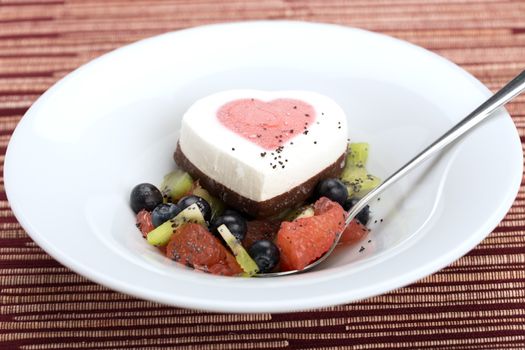 Heart ice cream with blueberry, grapefruit and kiwi on white plate.