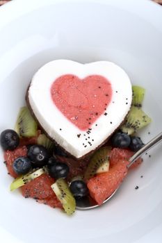 Heart ice cream with blueberry, grapefruit and kiwi on white plate.