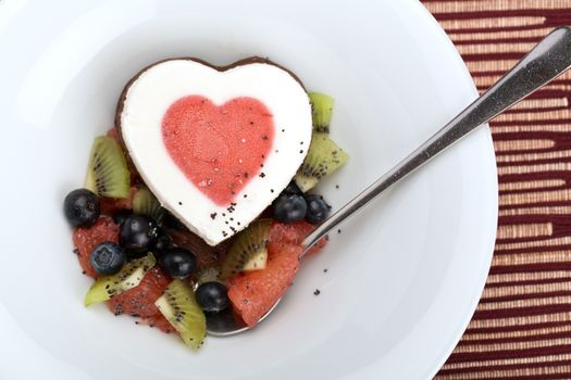 Heart ice cream with blueberry, grapefruit and kiwi on white plate.