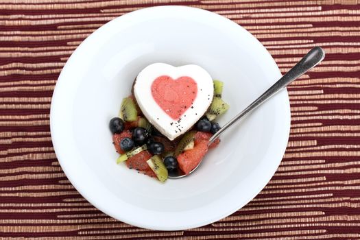 Heart ice cream with blueberry, grapefruit and kiwi on white plate.
