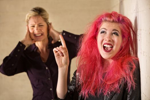 Woman covering ears while woman in pink hair sings