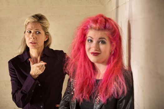 Concerned mother pointing at grinning daughter in pink hair