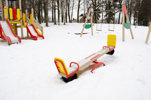 empty colorful playground surrounded by snow in winter. swing and other leisure equipment for children.