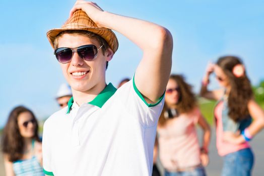 young man in sunglasses, a hat holds a hand on a background of blue sky and friends