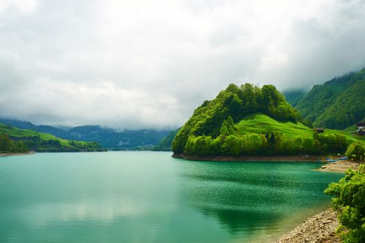 Beautiful emerald mountain lake in Switzerland under low clouds
