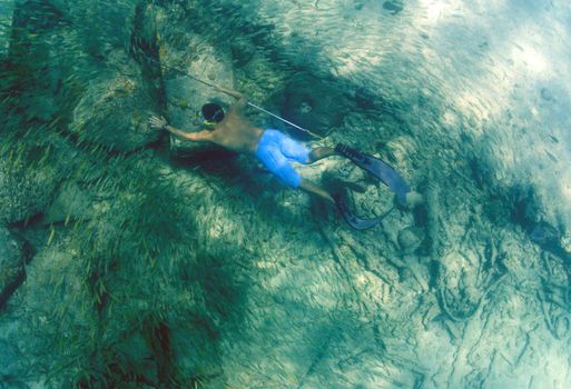 man spearfishing with spear pole underwater in bahamas